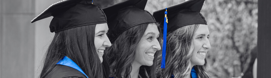 Three female graduates; in their CUW regalia, pose for a photo.